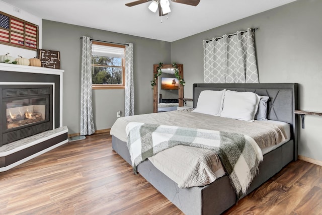bedroom with a glass covered fireplace, baseboards, a ceiling fan, and wood finished floors