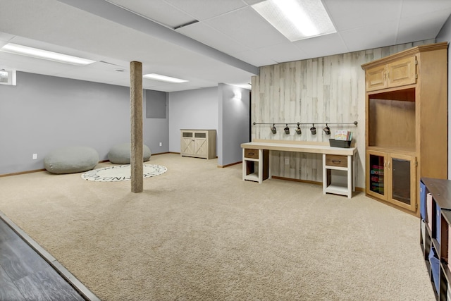 finished basement featuring baseboards, wood walls, a drop ceiling, and carpet flooring