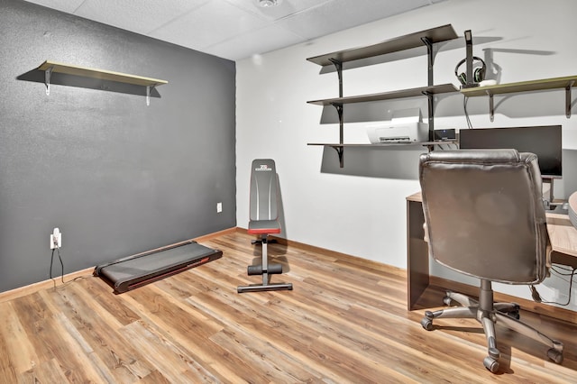 unfurnished office with baseboards, a drop ceiling, and wood finished floors
