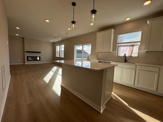 kitchen featuring white cabinets, a sink, a glass covered fireplace, wood finished floors, and a kitchen island