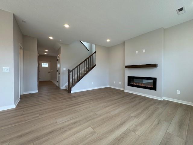 unfurnished living room with stairs, baseboards, visible vents, and wood finished floors
