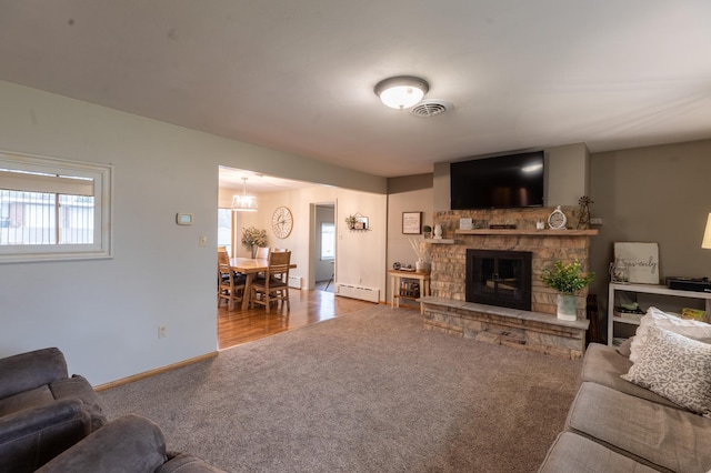carpeted living area with a fireplace, visible vents, plenty of natural light, and a baseboard radiator