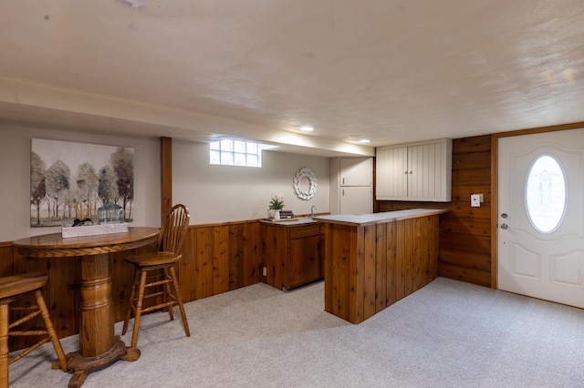 bar featuring wooden walls, a bar, wainscoting, and light colored carpet