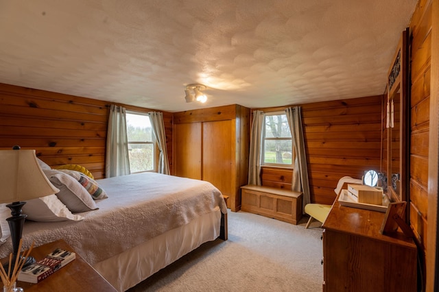 bedroom featuring a closet, wood walls, a textured ceiling, and light colored carpet