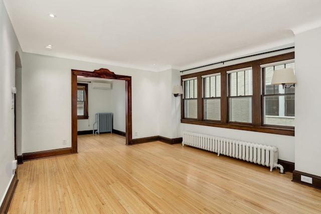 1287 Avon St N, Saint Paul, MN 55117 - spare room featuring radiator, light wood-style floors, baseboards, arched walkways, and recessed lighting