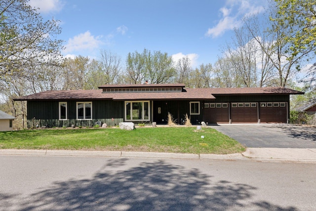 prairie-style home featuring an attached garage, aphalt driveway, a front lawn, board and batten siding, and roof with shingles