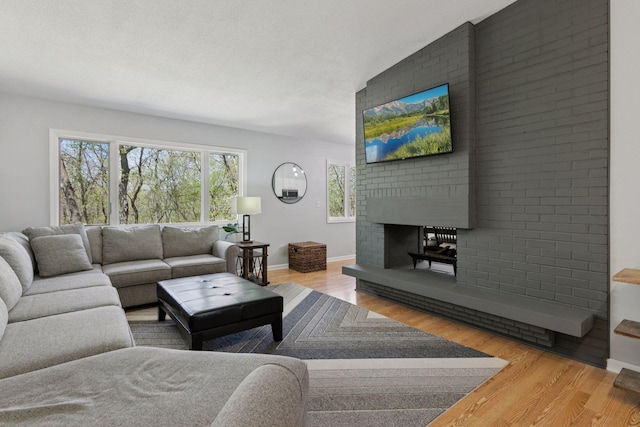 living area featuring a brick fireplace, baseboards, and wood finished floors