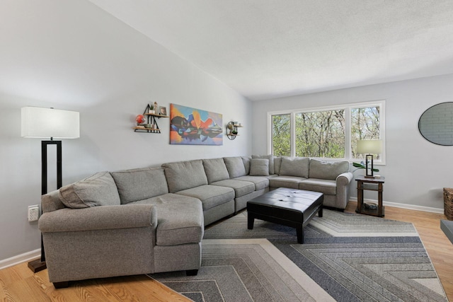 living room featuring baseboards, light wood-style floors, and lofted ceiling
