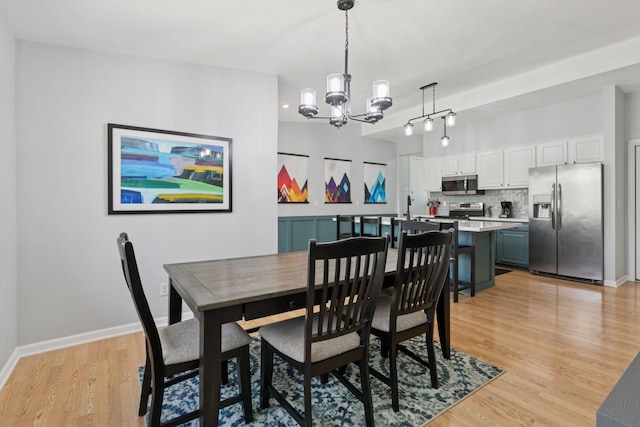 dining area with a chandelier, light wood-style flooring, and baseboards