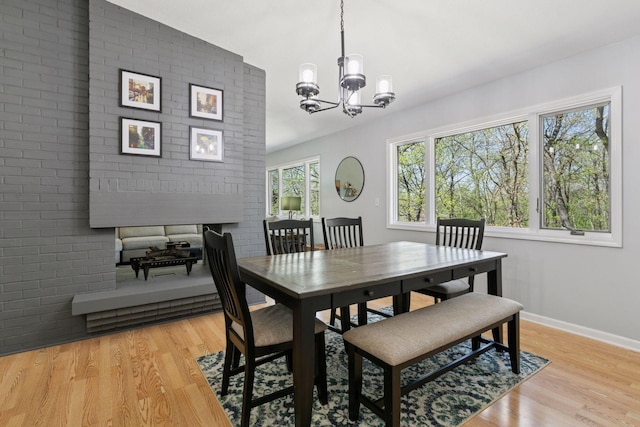 dining area with baseboards, a fireplace, an inviting chandelier, and light wood-style flooring