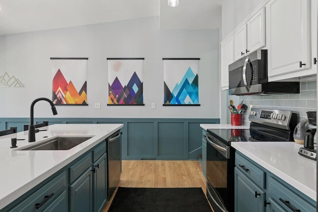 kitchen with a sink, light wood-type flooring, white cabinetry, light countertops, and appliances with stainless steel finishes