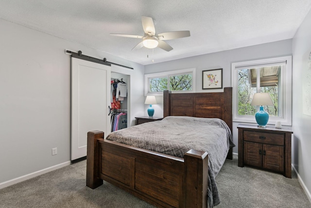 bedroom with carpet flooring, a closet, a barn door, baseboards, and ceiling fan