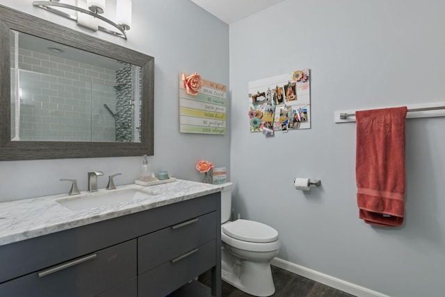 full bath featuring toilet, wood finished floors, a tile shower, baseboards, and vanity