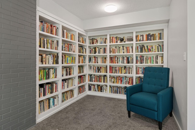 sitting room with wall of books, a textured ceiling, carpet flooring, and brick wall