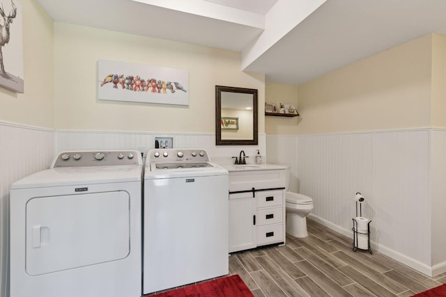 laundry room featuring wainscoting, washer and dryer, a sink, and wood finished floors
