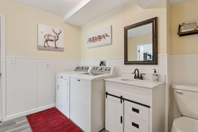 clothes washing area featuring light wood finished floors, wainscoting, a sink, washing machine and clothes dryer, and laundry area