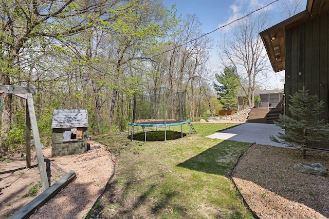 view of yard featuring an outdoor structure, a trampoline, a patio, a shed, and stairway