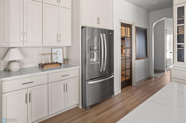 kitchen featuring baseboards, stainless steel refrigerator with ice dispenser, white cabinets, light stone counters, and light wood finished floors