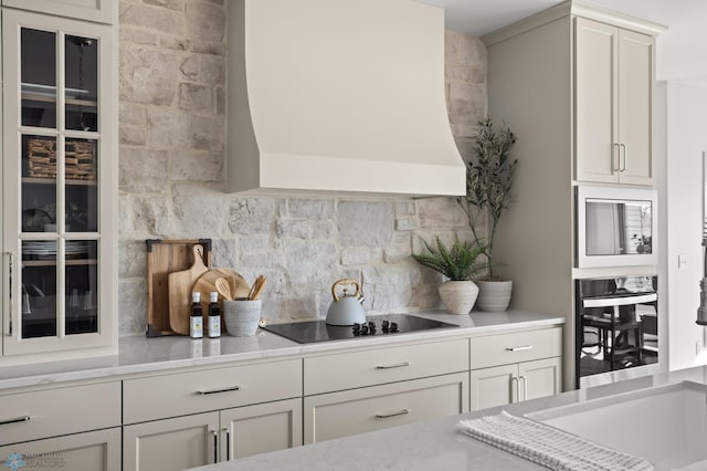 kitchen with tasteful backsplash, built in microwave, custom range hood, black electric stovetop, and stainless steel oven