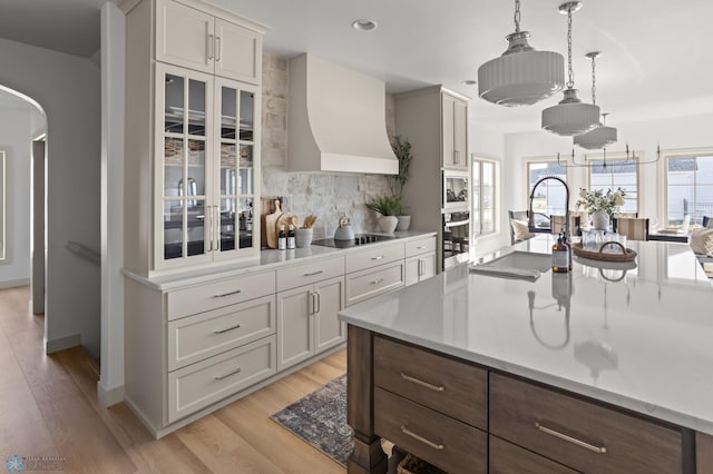 kitchen with backsplash, stainless steel oven, light wood-type flooring, and custom range hood