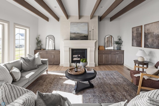 living room with baseboards, a glass covered fireplace, beam ceiling, and light wood finished floors