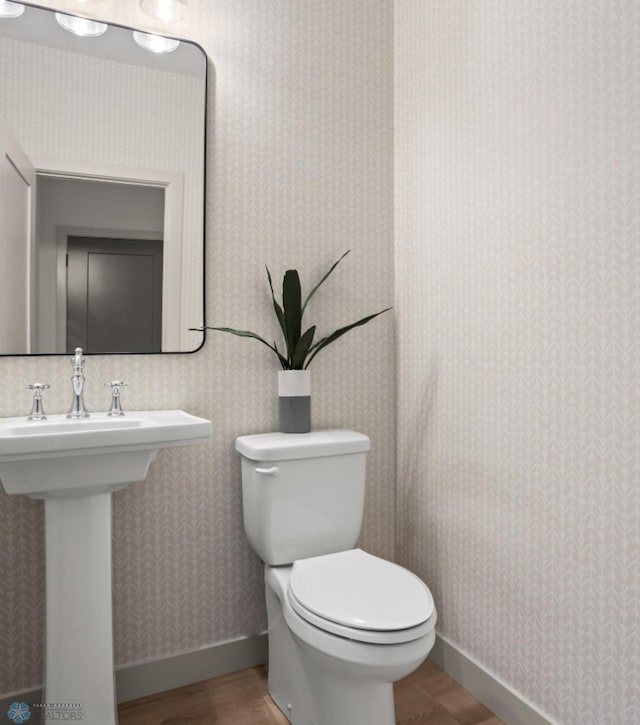 half bathroom with baseboards, wood finished floors, toilet, and wallpapered walls