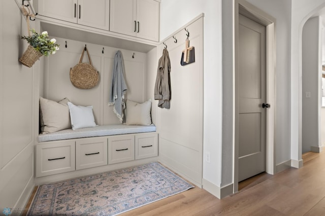 mudroom featuring arched walkways, baseboards, and light wood finished floors