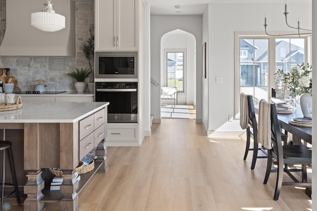 kitchen with arched walkways, built in microwave, stainless steel oven, and light wood-style flooring