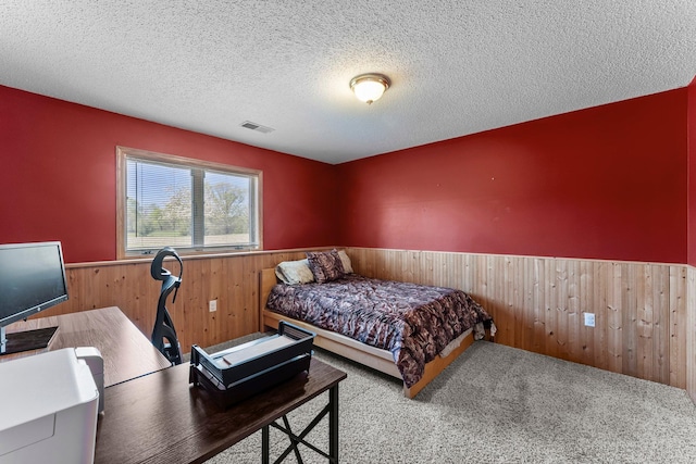 bedroom featuring a wainscoted wall, wooden walls, carpet floors, and a textured ceiling