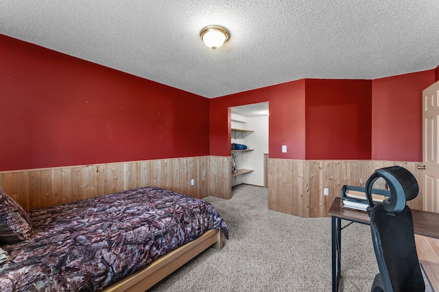 bedroom with wainscoting, carpet, wooden walls, and a textured ceiling