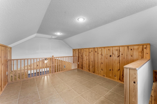bonus room with lofted ceiling, a textured ceiling, and wooden walls