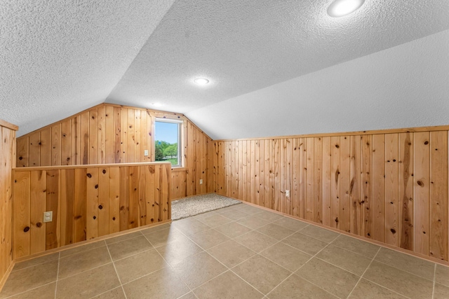 additional living space featuring a textured ceiling, lofted ceiling, and wooden walls