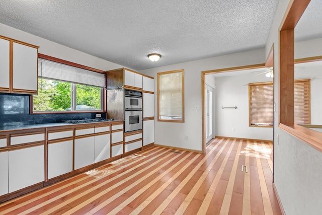 1791 Lois Dr, Shoreview, MN 55126 - kitchen featuring stainless steel double oven, white cabinets, light wood finished floors, a textured ceiling, and black stovetop