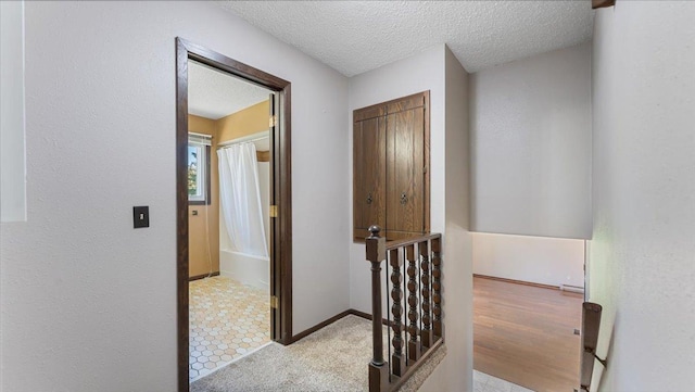 hall with a textured ceiling, an upstairs landing, and baseboards