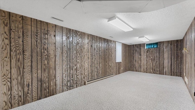 basement featuring a baseboard heating unit, wood walls, a textured ceiling, and carpet