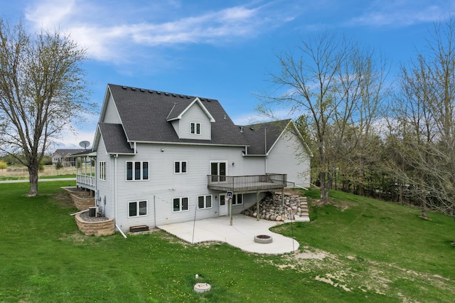 rear view of house featuring roof with shingles, a wooden deck, an outdoor fire pit, a yard, and a patio