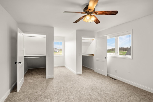 unfurnished bedroom featuring light colored carpet, visible vents, a ceiling fan, baseboards, and a spacious closet