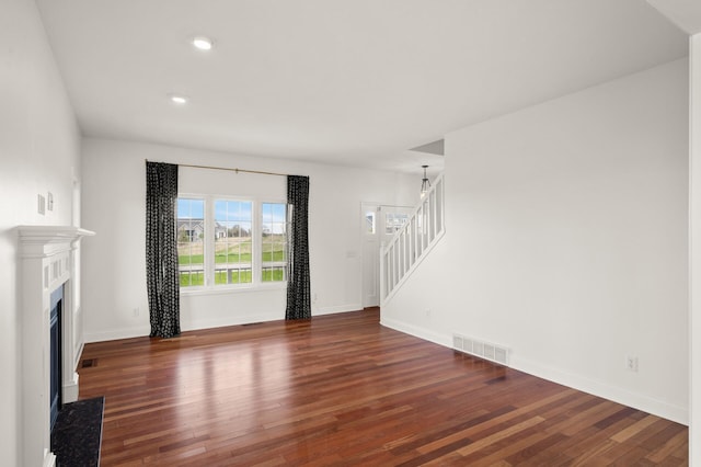 unfurnished living room with stairs, baseboards, a fireplace with flush hearth, wood finished floors, and visible vents