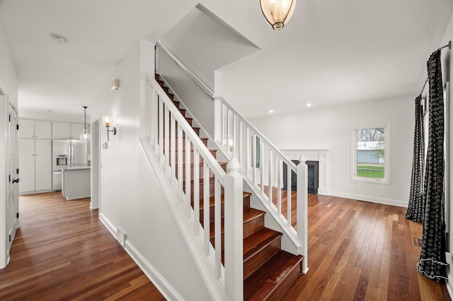 staircase featuring baseboards, recessed lighting, a fireplace, and hardwood / wood-style flooring