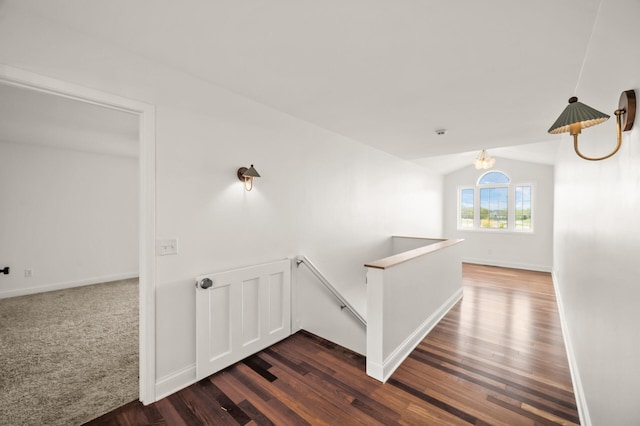 corridor featuring dark wood-style flooring, a notable chandelier, baseboards, an upstairs landing, and lofted ceiling