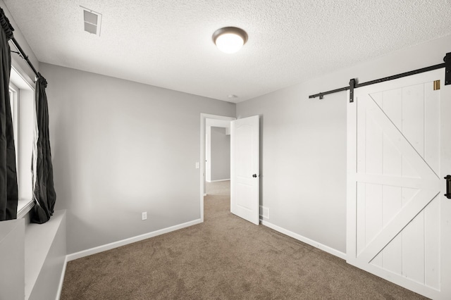 unfurnished bedroom featuring carpet flooring, a textured ceiling, visible vents, and a barn door