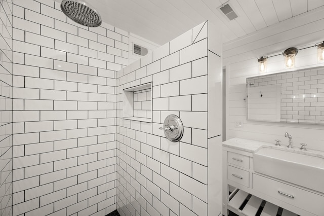 full bathroom featuring vanity, tiled shower, and visible vents