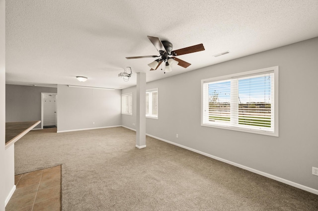 below grade area with a ceiling fan, a textured ceiling, visible vents, carpet floors, and baseboards