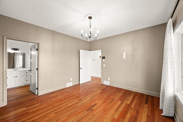 unfurnished bedroom with a notable chandelier, light wood-style floors, baseboards, ensuite bathroom, and visible vents
