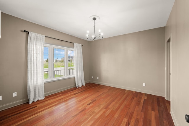 spare room featuring baseboards, an inviting chandelier, and light wood-style floors