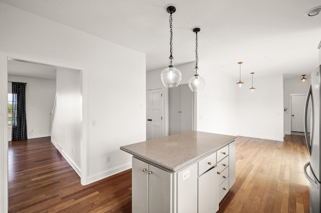 kitchen featuring wood-type flooring, pendant lighting, freestanding refrigerator, a kitchen island, and baseboards
