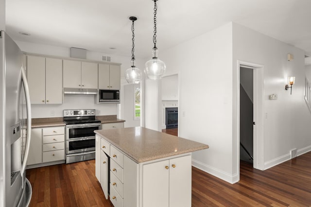 kitchen featuring under cabinet range hood, stainless steel appliances, dark wood finished floors, and a kitchen island