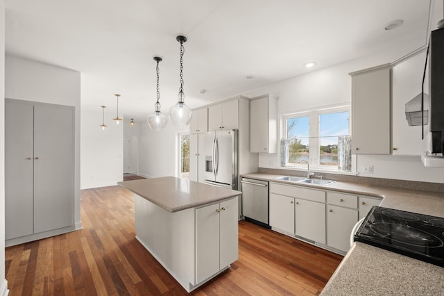 kitchen featuring a center island, hanging light fixtures, wood finished floors, a sink, and stainless steel appliances