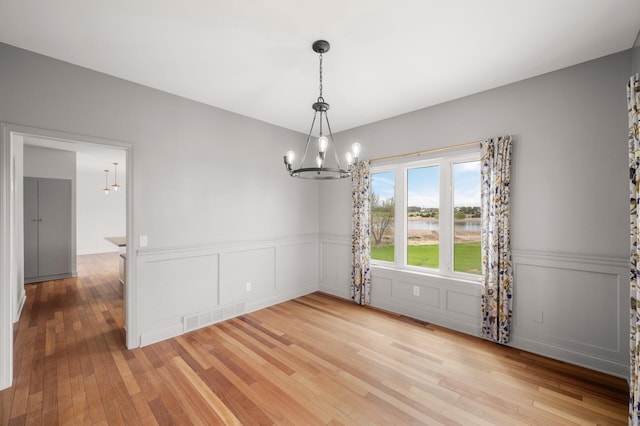 unfurnished dining area with visible vents, wainscoting, light wood-style floors, a water view, and a notable chandelier