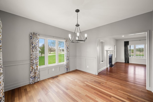 unfurnished dining area featuring a notable chandelier, wainscoting, light wood-style floors, a fireplace with flush hearth, and visible vents